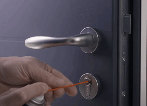 une personne qui lubrifie le barillet de sa porte d'entrée avec un lubrifiant pour serrure