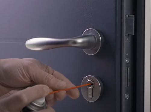 une personne qui lubrifie le barillet de sa porte d'entrée avec un lubrifiant pour serrure